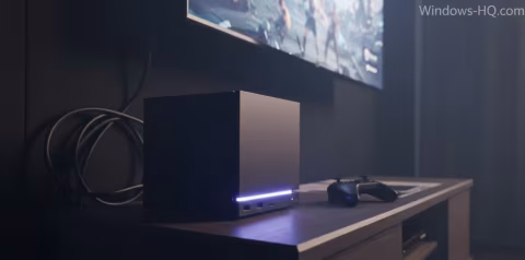 A black mini PC with blue lighting sits on a desk in front of a glowing screen.