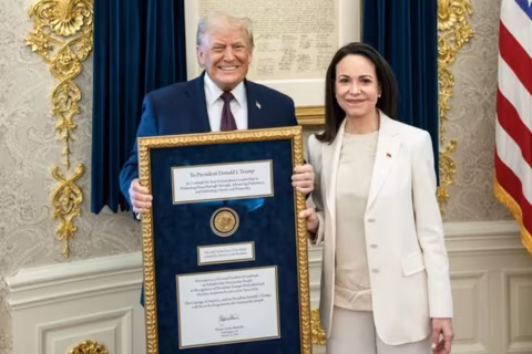 A man and a woman stand, holding a framed document that reads 'To President Donald J. Trump'.