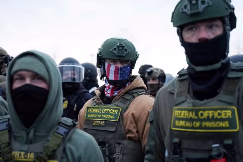 Three federal officers in tactical gear stand outdoors in an open area.