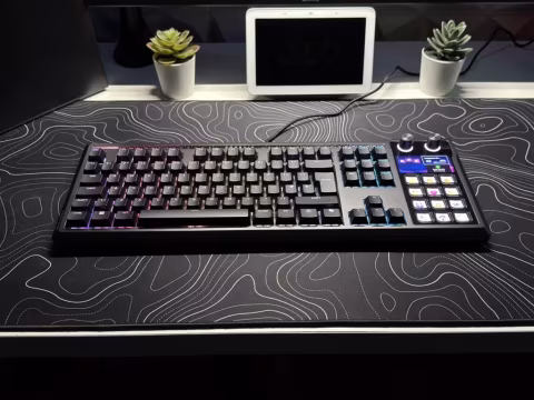 A large mechanical keyboard with an integrated touchscreen display sits on a patterned surface.