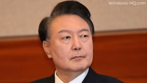 A middle-aged East Asian man in a dark suit is captured indoors.