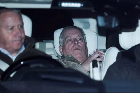 Two men seated in a car, one looking left and the other looking forward.