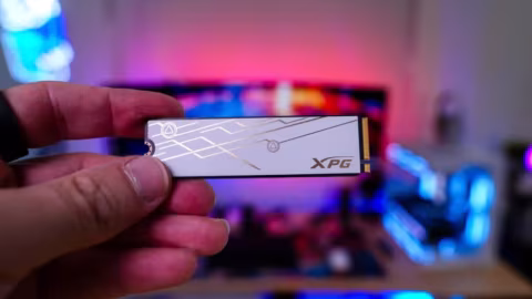 A person holds a white M.2 solid-state drive with gold and black accents.