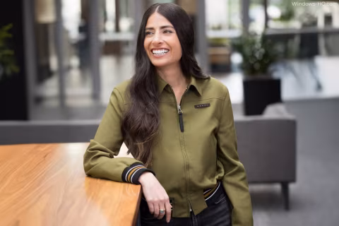 Young woman with dark hair smiling while seated at a wooden table.