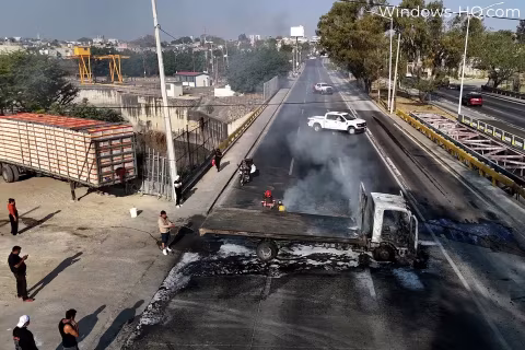 Vehicles and people gathered at an elevated road crossing in a partially urban area.