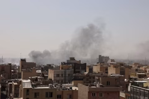 A view of buildings with large smoke plumes in the background.