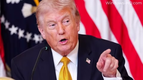 A man in a suit with blond hair gestures with his right hand while speaking at a podium.