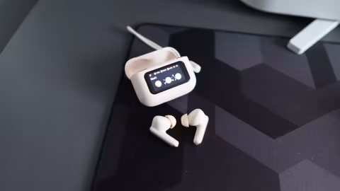 Wireless earbuds and charging case with a display screen on a dark surface.