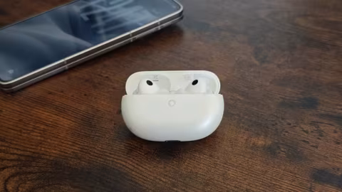 White wireless earbuds case and a dark smartphone lying on a wooden surface.