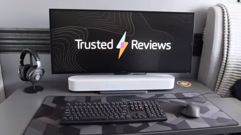 A computer monitor displays the text 'Trusted Reviews' on a desk with a keyboard and headphones.