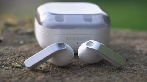 A pair of white wireless earbuds and their charging case resting on textured stone.