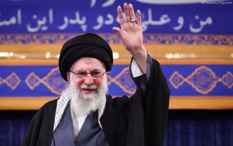 A man with a turban and beard raises his right hand in a wave.