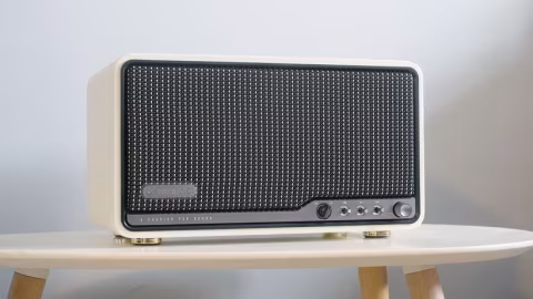 A rectangular audio speaker unit with a silver faceplate and visible controls, resting on a wooden surface.