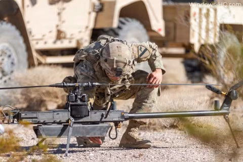 Soldier kneeling next to a long, unmanned aerial vehicle system in a field.