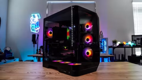 A large, black computer case with curved glass panels and internal RGB lighting, shown on a wooden desk.