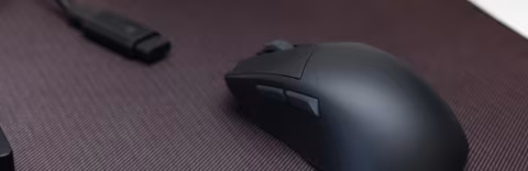 A dark, ergonomic gaming mouse and a black USB receiver are on a textured, dark surface.