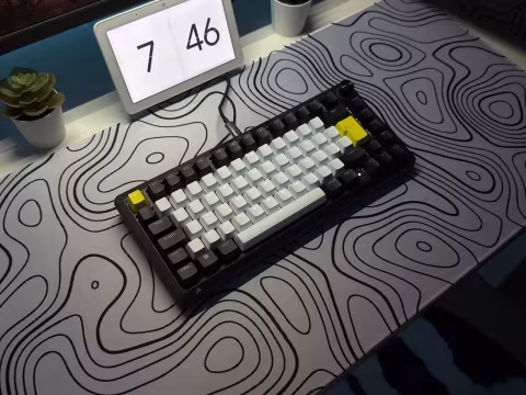 A compact mechanical keyboard and a digital display unit resting on a patterned surface.