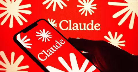 A hand holds a smartphone displaying the word Claude on a red background.
