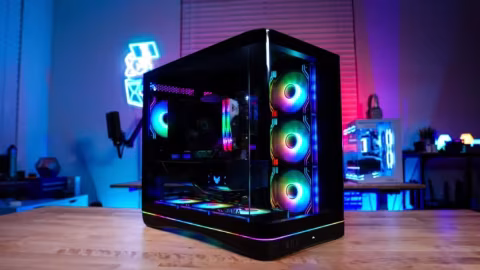 A black PC case with glass panels and RGB lighting sits on a wooden surface.