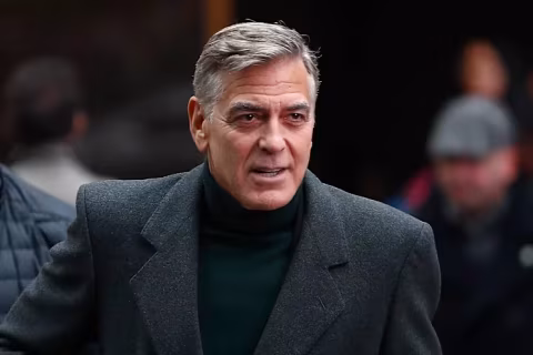 Middle-aged man with gray hair and dark coat standing outdoors.