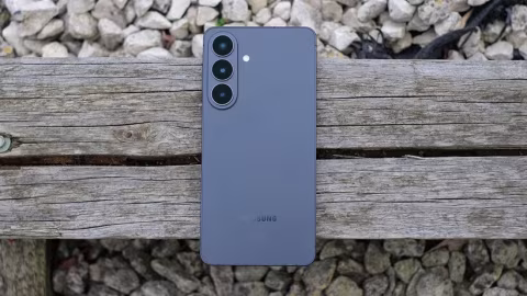 A light gray smartphone with a large camera array is positioned on weathered wooden planks.