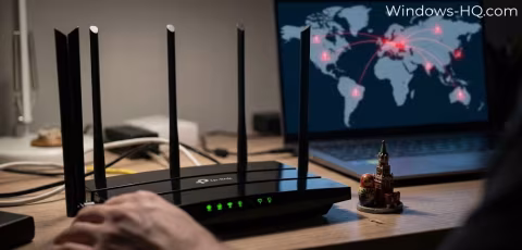A black Wi-Fi router with multiple antennas sits on a desk next to an open laptop screen showing a world map.