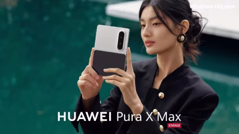 A woman holding a black foldable smartphone, featuring the Huawei logo, in a green outdoor setting.