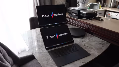 Two laptops open on a glass table with the text "Trusted Reviews" displayed on the screens.