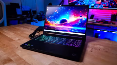 A laptop computer is open on a wooden desk, displaying a cosmic image on its screen.