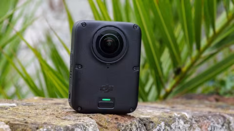 A black 360-degree camera device rests on a rough, textured stone surface outdoors.