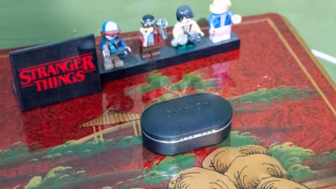 Grey electronic device on a patterned surface in front of action figures and a black sign reading Stranger Things.