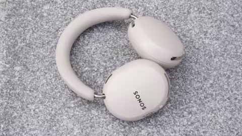 Two white wireless earbuds, one inside its charging case, resting on a textured gray surface.
