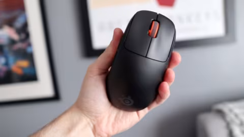 A hand holding a matte black, ergonomic wireless mouse with a colored accent and visible logo.