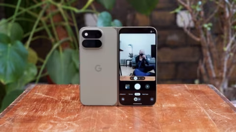 Two smartphones, one standard and one foldable, are displayed side-by-side on a wooden table.