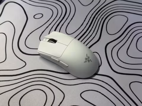 A white wireless mouse rests on a light grey surface patterned with wavy black lines.