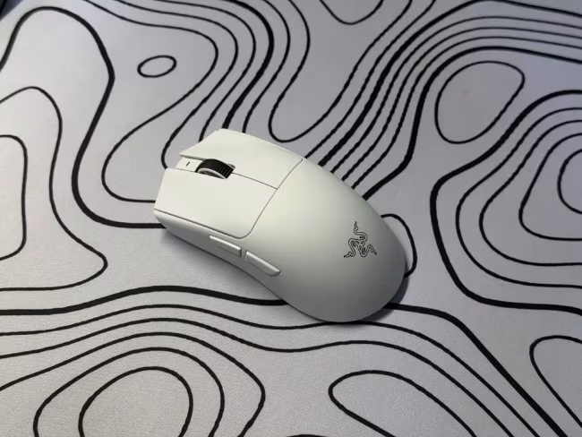 A white wireless mouse rests on a light grey surface patterned with wavy black lines.