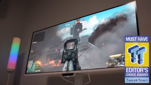 Ultrawide monitor displaying a bright video game screenshot featuring explosions, structures, and action.