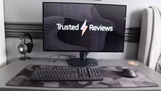A monitor displaying the words 'Trusted Reviews' and a lightning bolt, resting on a desk setup with a keyboard and mouse.