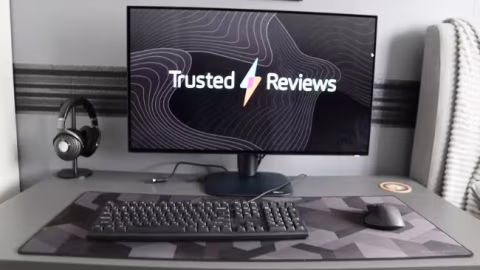 A monitor displaying the words 'Trusted Reviews' and a lightning bolt, resting on a desk setup with a keyboard and mouse.