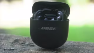 Black charging case for wireless earbuds displaying "BOSE," placed on a rough, gray surface.