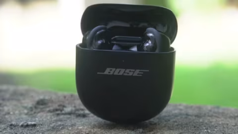 Black charging case for wireless earbuds displaying "BOSE," placed on a rough, gray surface.