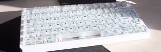 A light-colored, compact mechanical keyboard displaying a standard alphanumeric key layout.