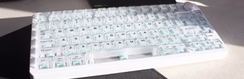 A light-colored, compact mechanical keyboard displaying a standard alphanumeric key layout.