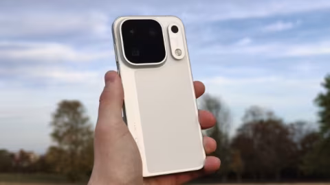A light cream-colored smartphone held vertically in a hand, set against an outdoor background.