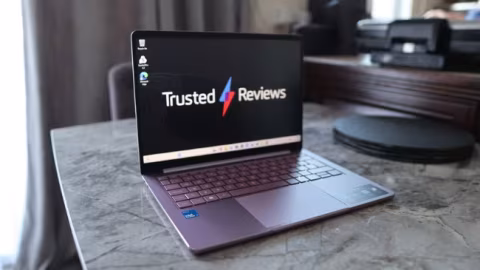 A laptop displaying the 'Trusted Reviews' logo, resting on a textured gray surface.