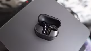 A pair of wireless earbuds inside a dark charging case, resting on a light gray surface.